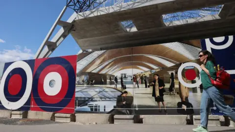 Getty Images A woman walks by a picture showing what the inside of a new rail terminal will look like on the outside of the partly-built building of the Rail Baltica Riga central hub in Riga, Latvia