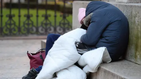 PA Media Two homeless people sleeping on a stone bench