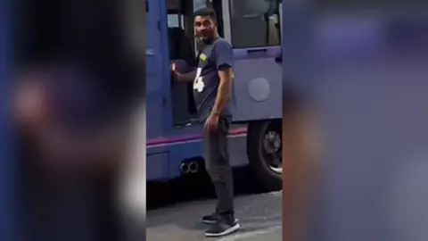 West Yorkshire Police A man in dark trousers and a blue t-shirt holds a lit flame to the back seat of a bus