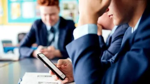 Getty Images Anonymous pupils in a classroom staring at their mobile phone screens