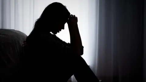 Getty Images Silhouette of an anonymous woman sat looking distressed