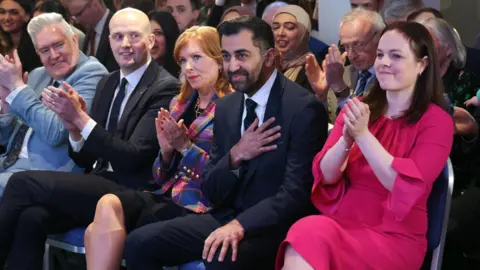 EPA Humza Yousaf holding his chest and smiling after being elected SNP leader. Kate Forbes is to his right, Ash Regan and Stephen Flynn to his left. 
