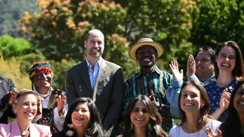 Reuters Prince William smiles in a group photo with the finalists of the 2024 Earthshot Award. Seven women and three men surround him, they are all smiling and applauding.