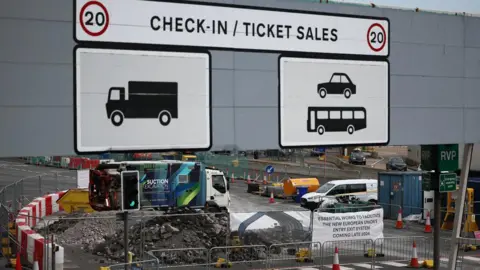 Getty Images A sign which reads check-in/ticket sales and has pictures of cars and lorries to show which lanes to use. Underneath and in the background you can see construction work going on with a pile of rubble, skips and machinery around