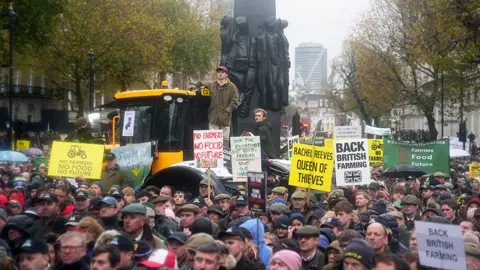 PA Media Crowd of protesters  holding banners including two on a yellow tractor a tractor holding banners stand in Whitehall in London