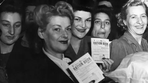 Getty Images Black-and-white photograph of women in the 1940s holding up their ration books.  