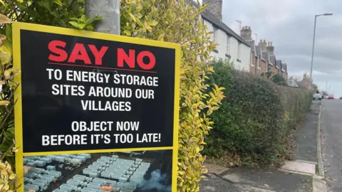 BBC A large sign saying 'Say No to Energy Storage' at the entrance to a village street