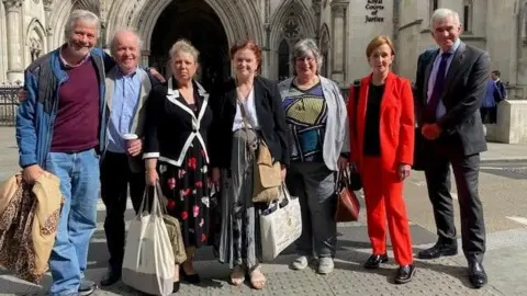 St Albans: Fight the Freight Four men and three women outside the stone-built Royal Courts of Justice in the Strand, London. They are carrying bags and rucksacks and standing in a line with the entrance to the court in the background. One is wearing a red jacket and trousers.