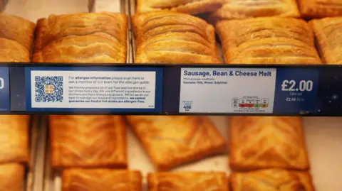 Reuters A range of baked savoury products can be seen on display in a Greggs store, with signs including 'freshly baked', 'adults need around 2000kcal a day', 'vegan festive bake' and 'cheese and onion bake'.