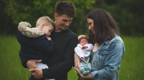 PA Real Life/PA Sophie and her husband holding their two boys in their arms in a field smiling at each other