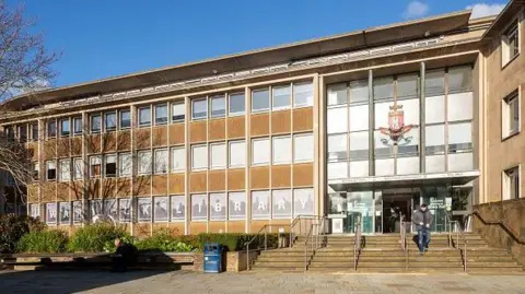 Getty Images A large flat roofed building with a mostly glass facade. There is an entrance with stairs leading to it on the right side, above the entrance is a coat of arms