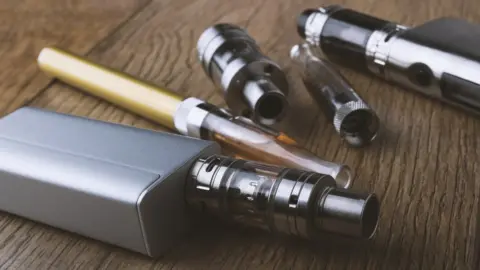 Getty Images A vape pen and different components of an e-cigarette on a wooden background