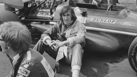 Joe Bangay Jackie Stewart sitting next to his car, a March-Cosworth 701, before the British Grand Prix held at Brands Hatch in July 1970