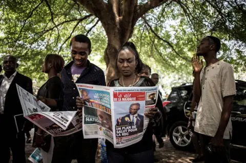AFP Supporters of the official DRCongo Presidential candidate, Emmanuel Ramazani Shadary, read a newspaper outside the Cathedral Notre-Dame Du Congo in Kinshasa on November 24, 2018, during the launch of his official electoral campaign.