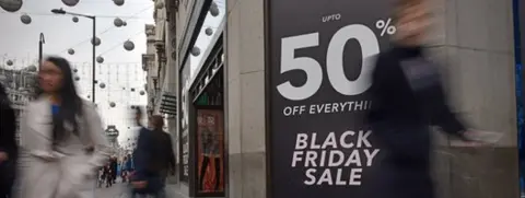 Shoppers walk past a sign in London advertising a Black Friday sale