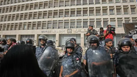 Getty Images Lebanese security forces secure the entrance of the Central Bank after anti-government protesters broke down a construction barrier as they rally at the same time of a press conference held by the bank's governor in Beirut on November 11, 2019.