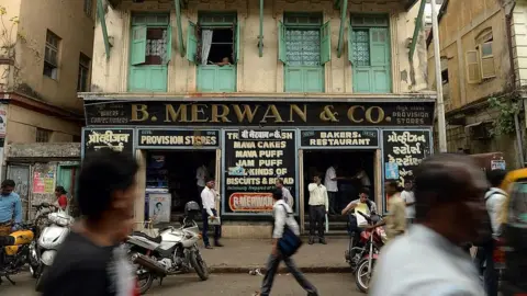 Getty Images Indian pedestrians walk past the B. Merwan & Co. Irani cafe in Mumbai