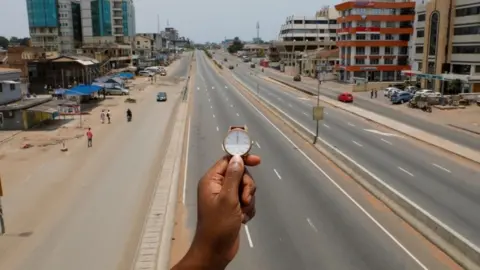 Reuters A watch showing the time at noon, is displayed for a photo as people walk past Ring Road Central Street, which is almost empty during the coronavirus disease (COVID-19) outbreak, in Accra, Ghana, March 31, 2020