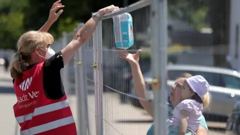 EPA A worker hands nappies over a fence to a person in quarantine in the German city of Guetersloh, June 2020