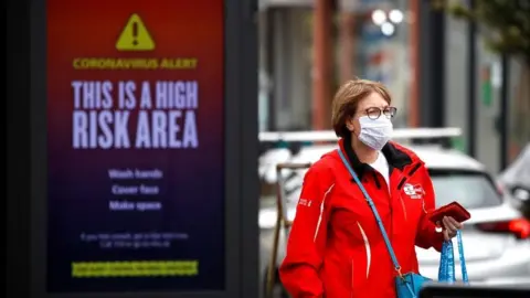 Reuters A woman wearing a protective mask walks past a warning sign in Greater Manchester