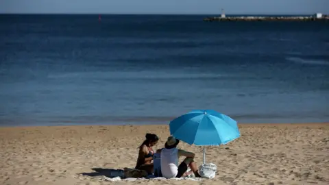 PA Media People enjoy the sun at the beach in Cascais, Portugal