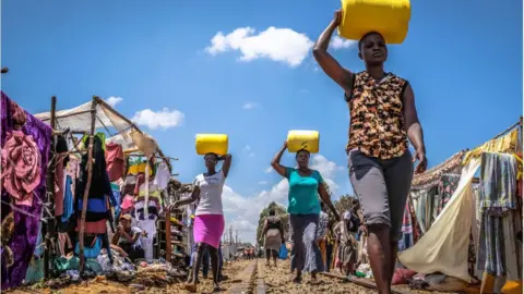 Getty Images Women walk back home carrying water cans in Kibera