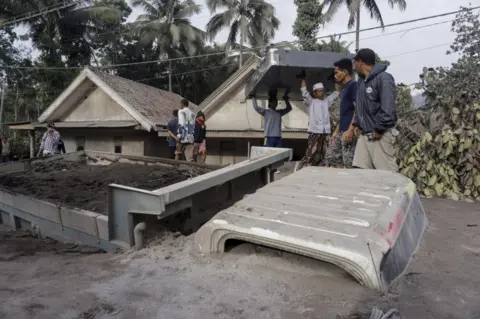 EPA Villagers carry their belongings near a truck buried under ash from Mt Semeru at Sumber Wuluh village in Lumajang, East Java, Indonesia, on 5 December 2021.