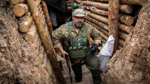 Getty Images Ukrainian soldier looks out from a trench in Donbas