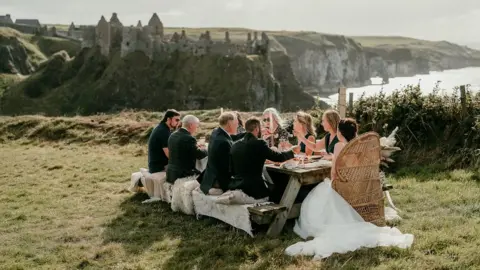 Epic Love Photography  Jamie and Corey with guest enjoying a picnic overlooking Dunluce Castle