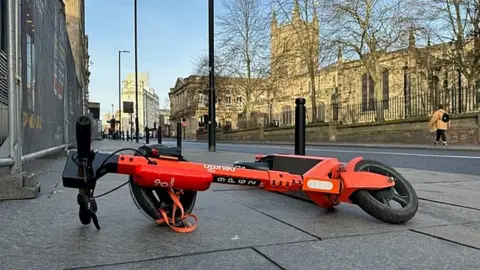 NFBUK A scooter lying on its side int he middle of the pavements