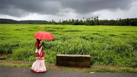 Getty Images A women waits in the rain for the public bus with the lush vegetation in back ground August 20, 2006 in Goa, India
