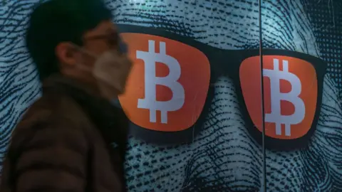 Getty Images Pedestrians walk past a display of cryptocurrency Bitcoin on February 15, 2022 in Hong Kong, China.