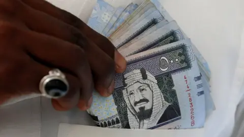 Reuters A Saudi man shows Saudi riyal banknotes at a money exchange, in Riyadh, Saudi Arabia (30 January 2016)