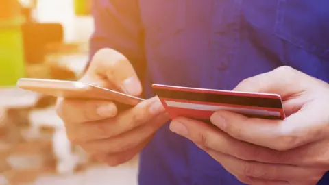 Getty Images Man holding credit card and phone