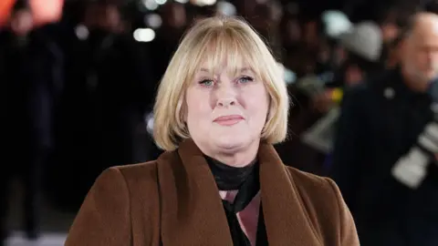 PA Media Sarah Lancashire at an outside event. She has blonde hair to her shoulders and is wearing a brown coat.