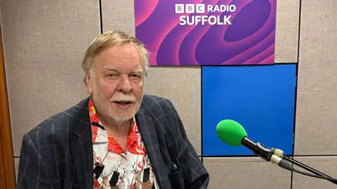 BBC Rick Wakeman sitting at a piano in the BBC Radio Suffolk studio looking into the camera