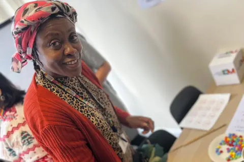 Jon Wright/BBC Nellie Kuma using chopsticks to move small sweets. She is wearing a red cardigan and a headband, as well as a leopard print top