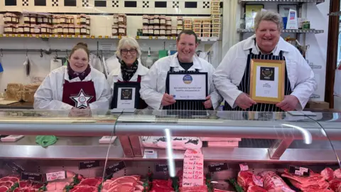 BBC / Luke Knight Tim Potter and his team standing behind butcher counter with awards. 