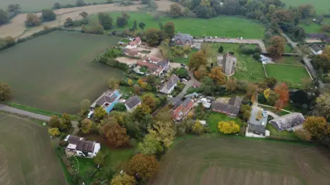 Qays Najm/BBC Aerial view of the village of Gissing, surrounded by fields and a large cluster of farm buildings including some houses and farm sheds as well as the parish church.
