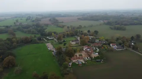 Qays Najm/BBC Aerial view of the village of Gissing, surrounded by fields and a large cluster of farm buildings including some houses and farm sheds as well as the parish church.