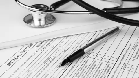 Getty Images A pen and a stethoscope lie on top of a sheet of paper saying medical history. 