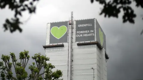 Reuters File image of Grenfell Tower covered by tarpaulin and scaffolding, with the grey and green 'Grenfell - forever in our hearts' sign at the top 