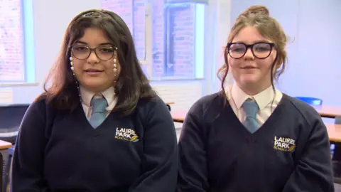 BBC Two teenage girls, both wearing glasses, sitting side by side in a school classroom