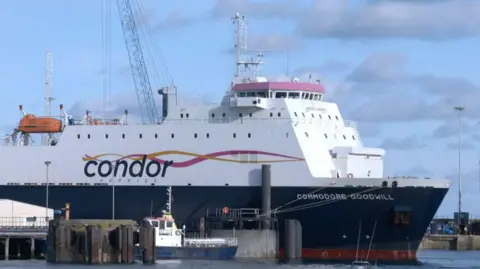 BBC A large Condor shipping vessel, top half white and bottom half navy blue, with a large Condor Ferries sign on the side, docked at the harbour.