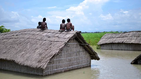 Getty Images Children sit on the roof of a submerged home after a 2016 flood of the Brahmaputra River in South Kamrup, India (Credit: Getty Images)