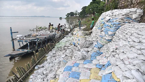 Getty Images Labourers pile sand bags to try to protect a bank of the Brahmaputra from erosion in Guwahati (Credit: Getty Images)