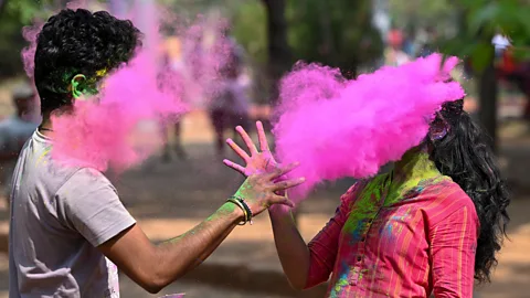 Getty Images Two people throw pink powder at each other during Holi