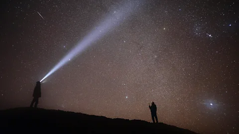 Getty Images Two people look up at a meteor streaking across a star speckled sky (Credit: Getty Images)