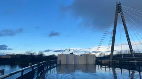 Claire Hamilton/BBC The boarded up boardwalk of Southport Pier with blue skies and wintry clouds
