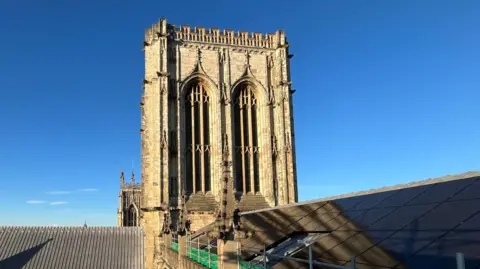 BBC/Julia Lewis Solar panels on the roof of York Minster, with the sun shining against a blue sky.